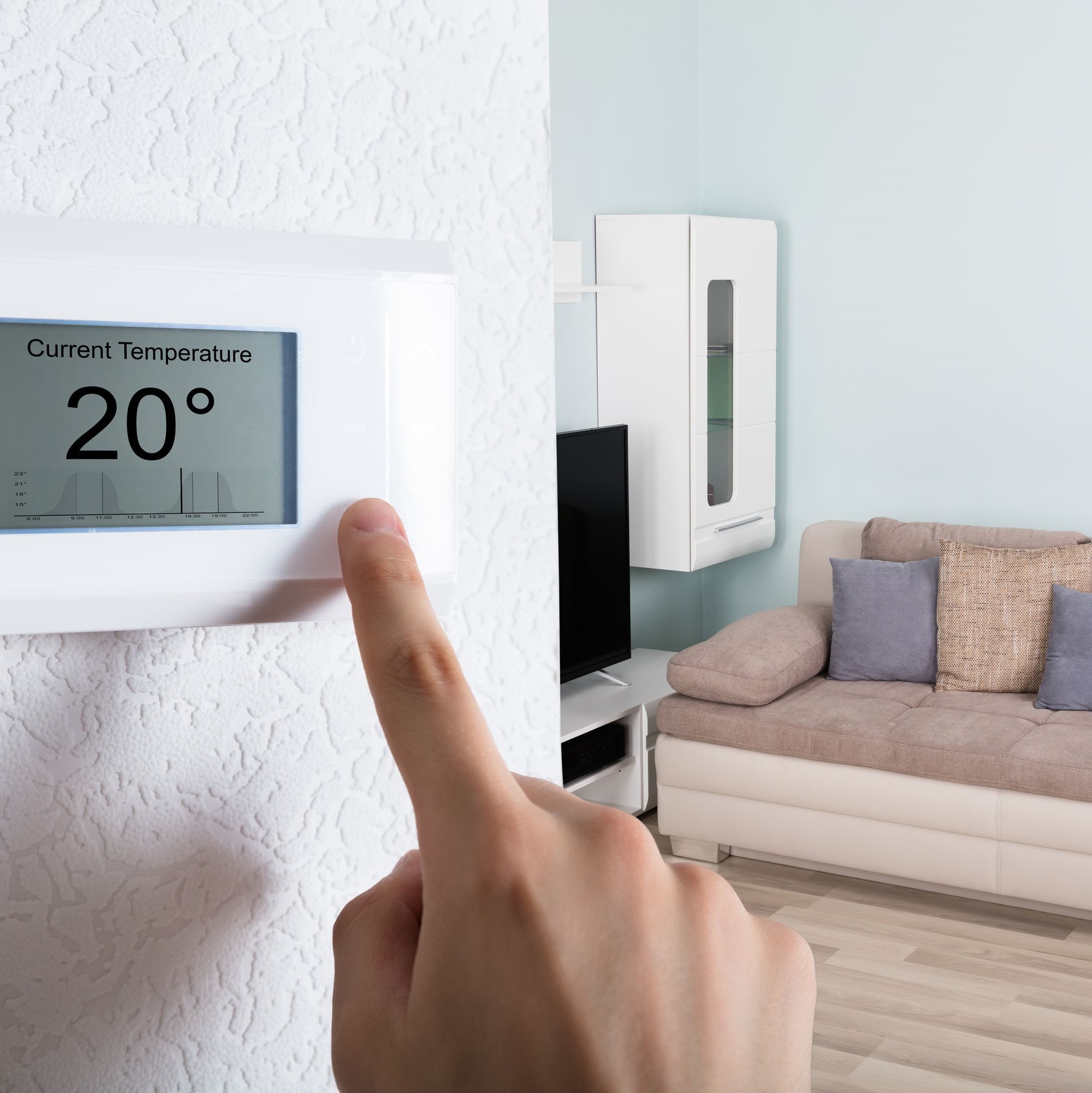 A finger on a thermostat inside a living room.